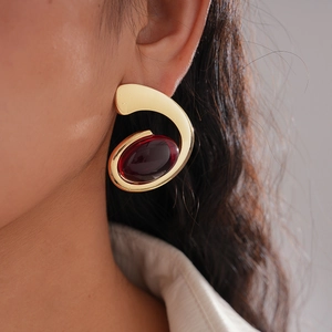Close-up of golden irregular earrings with deep red oval resin stones worn by model