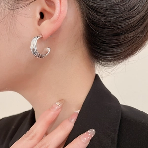 Close-up of silver wavy C-shaped acrylic earrings on model showing elegant metallic texture