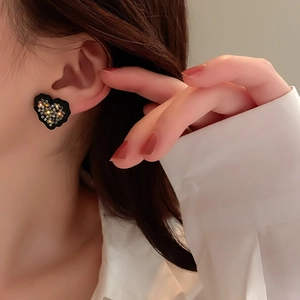 Détail d'une boucle d'oreille cœur noir sertie de strass portée par un mannequin