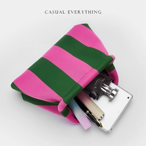 Pink and green striped knit clutch bag holding a tablet and cosmetics on white background