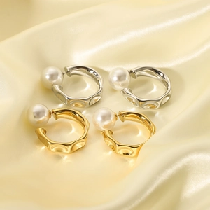 Irregular C-shaped gold and silver earrings with glossy white pearls on silk background