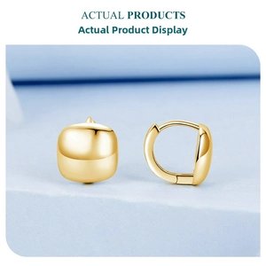 Detailed view of polished 18K gold plated silver huggie earrings on a light blue display