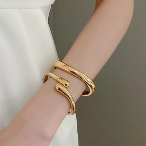 Detail shot of a minimalist gold open teardrop bangle and matching smooth round bracelet