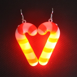 Close-up of heart-shaped candy cane LED earrings glowing in a festive red light