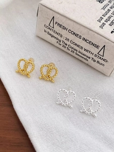 Detail of twisted knot bow earrings in gold and silver finish on textured fabric
