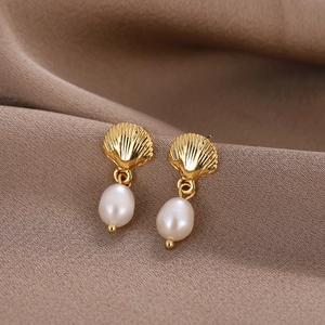 Close-up of golden shell stud earrings with white freshwater pearls on fabric