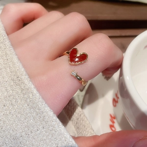 Detail of red enamel heart ring with zircon stone on finger with cozy coffee background