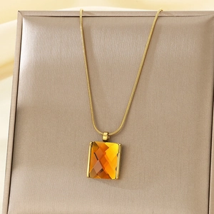Detailed macro of gold snake chain with faceted amber glass square pendant in a jewelry box