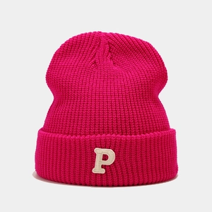 Detail of rose red chunky knit beanie featuring a white embroidered letter P patch