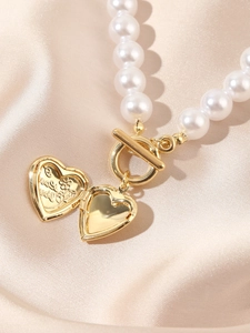 Detail of open gold heart locket with Love You engraving on white pearl necklace