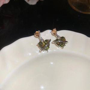 Macro view of olive green heart-shaped crystal earrings with silver planetary rings