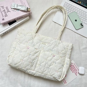Detailed top view of white quilted tote bag with heart embroidery and daily essentials