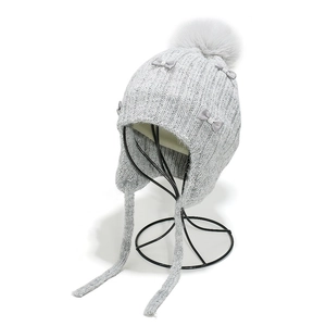 Detail of grey knitted earflap beanie featuring large pom-poms and small bow accents