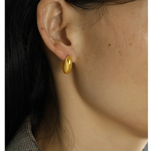 Close-up of minimalist golden bean stud earrings with high-polish finish on a model's ear