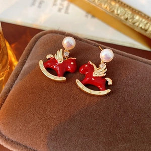 Macro view of red enamel rocking horse earrings with pearls and gold wing details