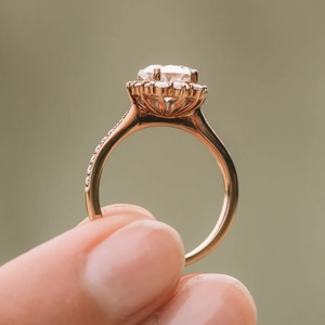 Rose gold engagement ring with oval clear stone and micro-pave diamonds held in hand