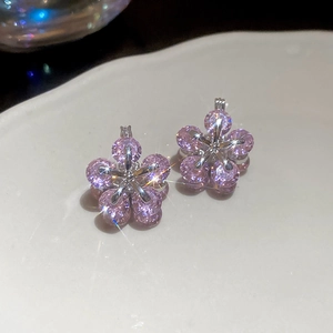 Macro shot of sparkling pink zircon flower earrings with silver prongs on white ceramic
