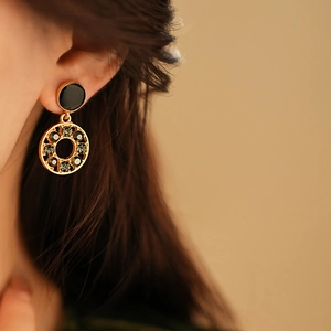 Détail de boucles d'oreilles dorées avec clous noirs et pendentifs circulaires