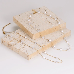 Elegant gold stainless steel chain necklace with integrated white pearls on stone display