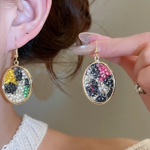 Close-up of elegant gold oval earrings set with colorful crystals on a female model