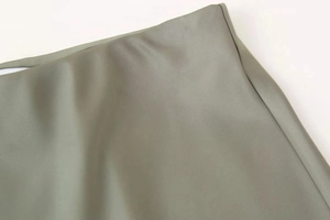 Close-up of olive green satin midi skirt fabric showing smooth texture and fine stitching