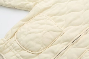 Detail of cream quilted jacket with large patch pockets and metal zipper closure