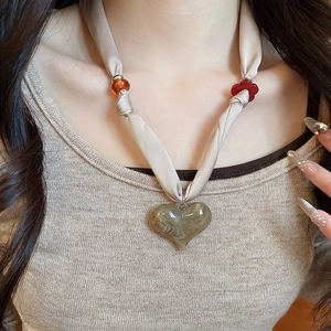 Close-up of heart acrylic pendant with red flower charm on fabric ribbon necklace