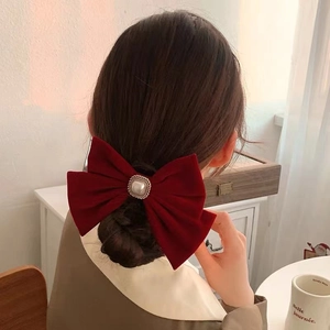Close-up of a large red velvet bow hair clip with a pearl center worn by a model