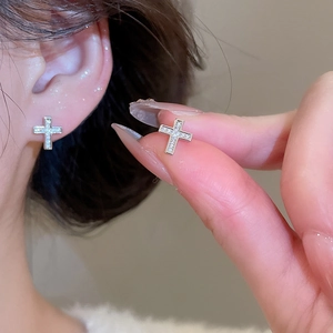 Close-up of silver cross stud earrings featuring pavé cubic zirconia on the ear