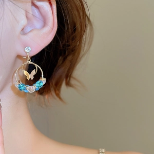 Close-up of gold butterfly hoop earring with blue and clear zircon crystals on ear