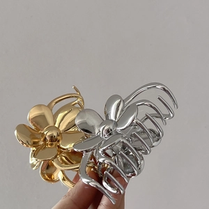Detail showing two floral metal hair claws in gold and silver finish being held
