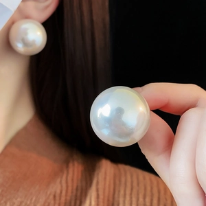 Detail showing oversized round pearl earring held by hand to highlight large scale