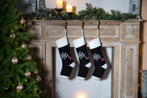 Three black knitted Christmas stockings with snowflake and candy cane hanging on fireplace