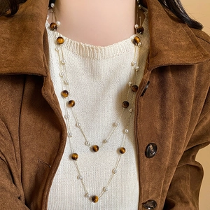 Détail d'un collier multicouche avec perles blanches et œil de tigre sur daim marron