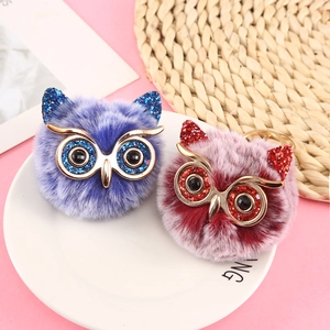 Close-up of colorful owl pom pom keychains with glitter eyes on a white ceramic plate