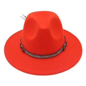 Detail of red wool fedora featuring a bohemian patterned band and feather accessory