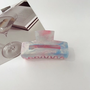Detailed view of pink and blue marble hair claw clip on a white desk with soft lighting