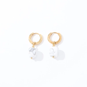 Close-up of geometric gold earrings with square white natural stone pendants and marble texture