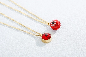 Detailed view of two gold necklaces with a red paved crystal ball and a single red gemstone