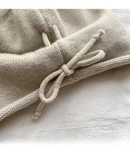 Detailed close-up of beige knitted beanie featuring a delicate drawstring bow texture