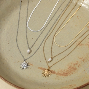 Layered gold and silver sun face necklaces with pearls on a vintage ceramic plate