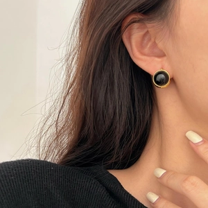 Close-up of minimalist black agate round earrings with gold trim worn by a model