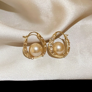 Close-up of golden U-shaped earrings with champagne rhinestones and lustrous pearls