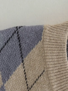 Detail of argyle knit vest featuring fuzzy texture and ribbed edges in grey and khaki