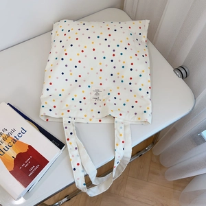 Close-up of white canvas tote bag with colorful polka dots and central fabric label