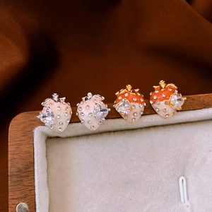 Détail macro de boucles d'oreilles fraise avec zircon en cœur et accents de strass