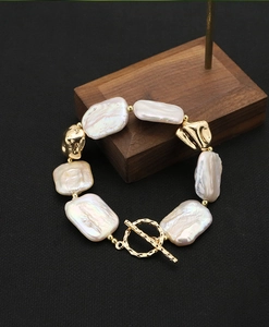 Detail of baroque pearl bracelet with 18k gold-plated OT toggle clasp on dark texture