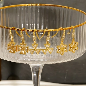 Three pairs of 18k gold earrings with zircon flowers and cross designs on a glass edge