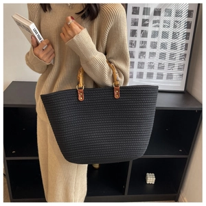 Detail of hand-woven black tote bag featuring a natural bamboo handle and gold rivets
