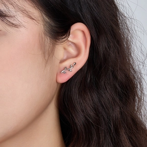 Detailed close-up of a silver leaf earring worn by a model in a natural setting